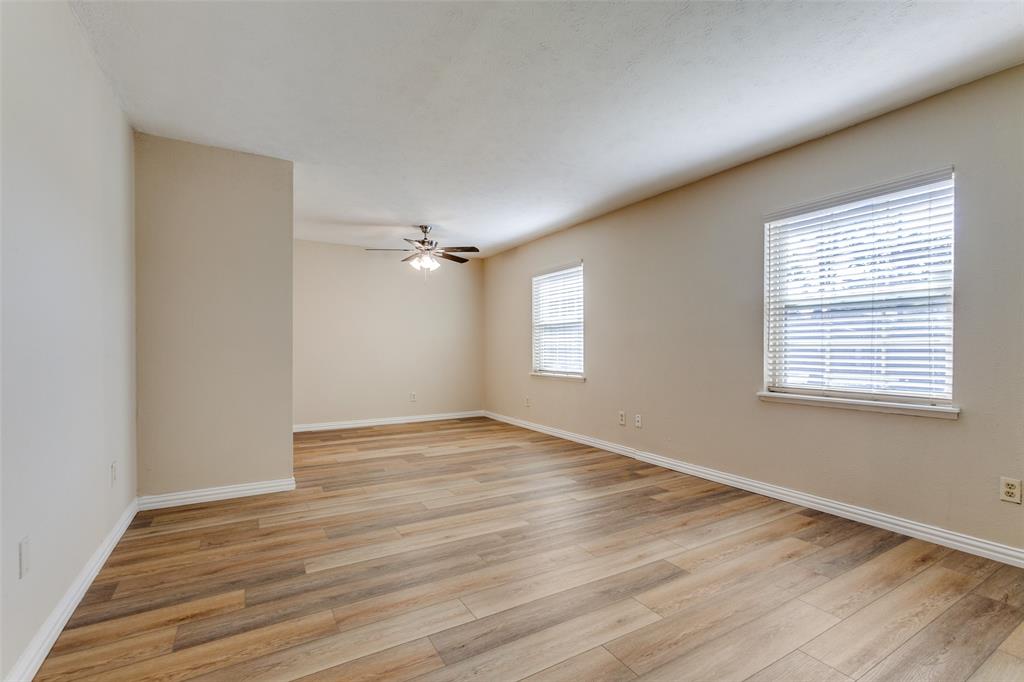 Wood-finish flooring, neutral wall tones, two windows with horizontal blinds, and a multi-blade ceiling fan with integrated lighting