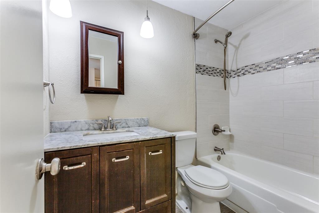 Bathroom featuring a vanity with stone countertop, drop-in sink, dark wood cabinetry, and a shower-tub combination with decorative tile inlay