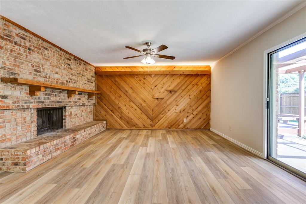 Living area featuring wood-finish flooring, a floor-to-ceiling brick fireplace with a custom wood mantel, diagonal wood-paneled accent wall, and a sliding glass door
