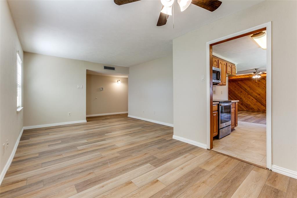 Open-concept area featuring wood-finish flooring, a ceiling fan, neutral wall paint, and natural illumination, with tile flooring visible in the kitchen