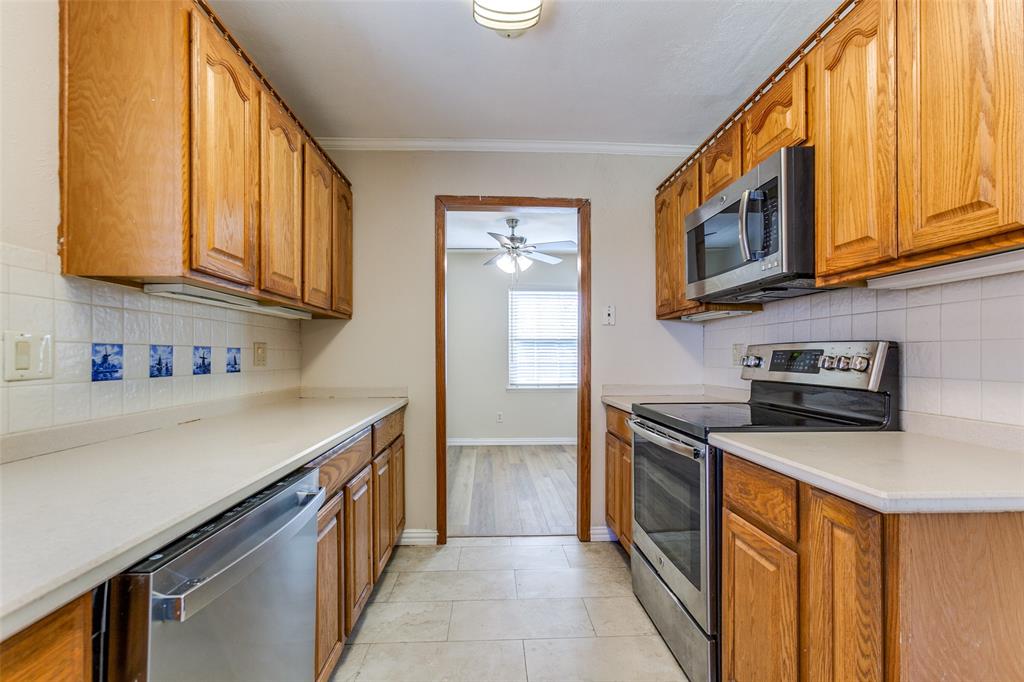 Kitchen featuring wood cabinetry, solid surface countertops, tiled backsplash with decorative accents, and stainless steel appliances including a range, microwave, and dishwasher