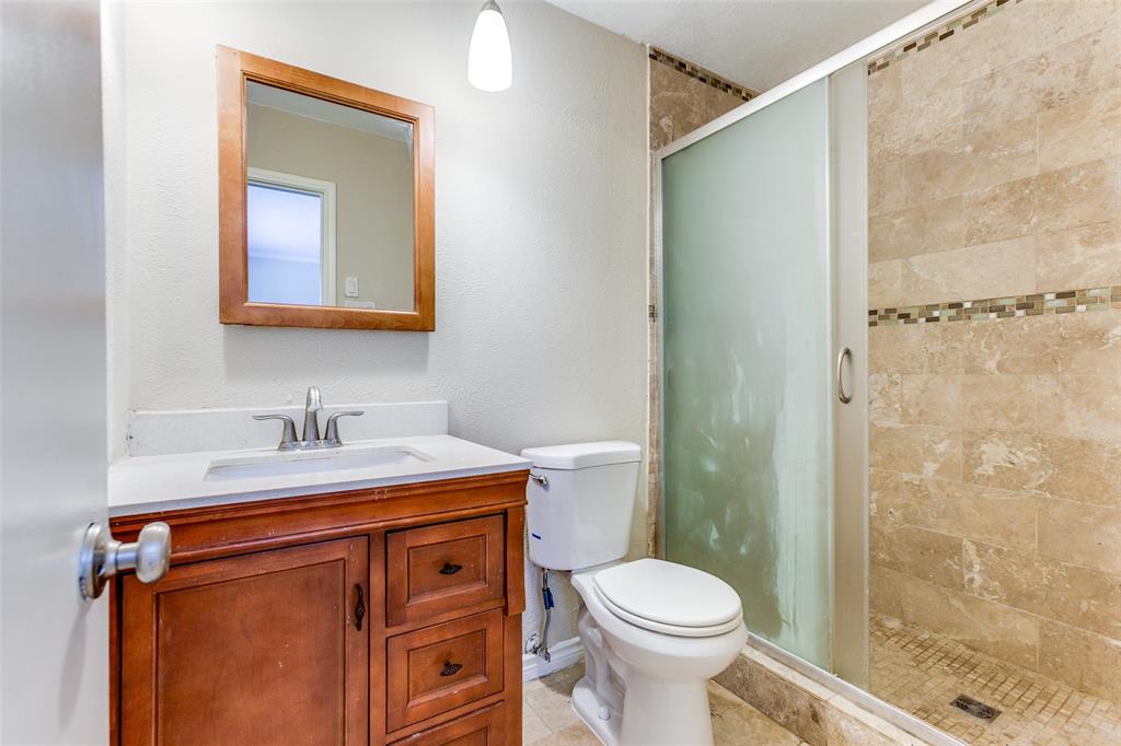 Bathroom vanity with wood-finish cabinetry, inset sink, framed wall mirror, and shower stall with tile surround and decorative stone-tile accent band