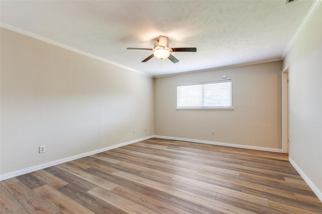 Neutral-toned interior space featuring wood-finish flooring, a ceiling-mounted light fixture with fan, and a window with horizontal blinds