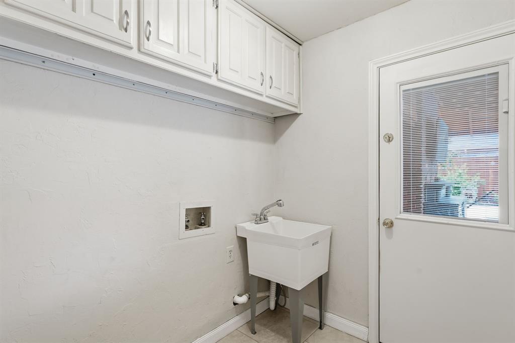 Laundry room offers a wash standalone sink and overhead cabinets.