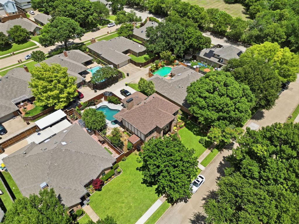 Aerial perspective of a multi-structure property featuring a swimming pool, multiple pitched shingle rooflines, mature trees, and landscaped lawn areas