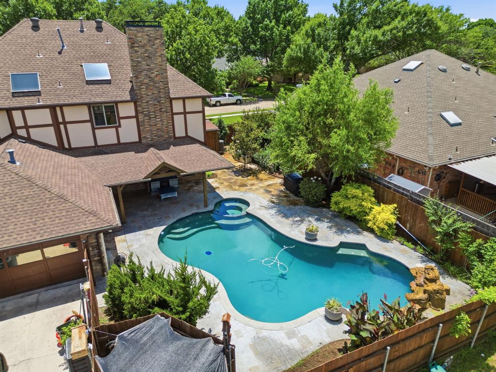 Backyard featuring an in-ground swimming pool with an integrated spa, stone masonry chimney, covered patio, and wood-finish garage door