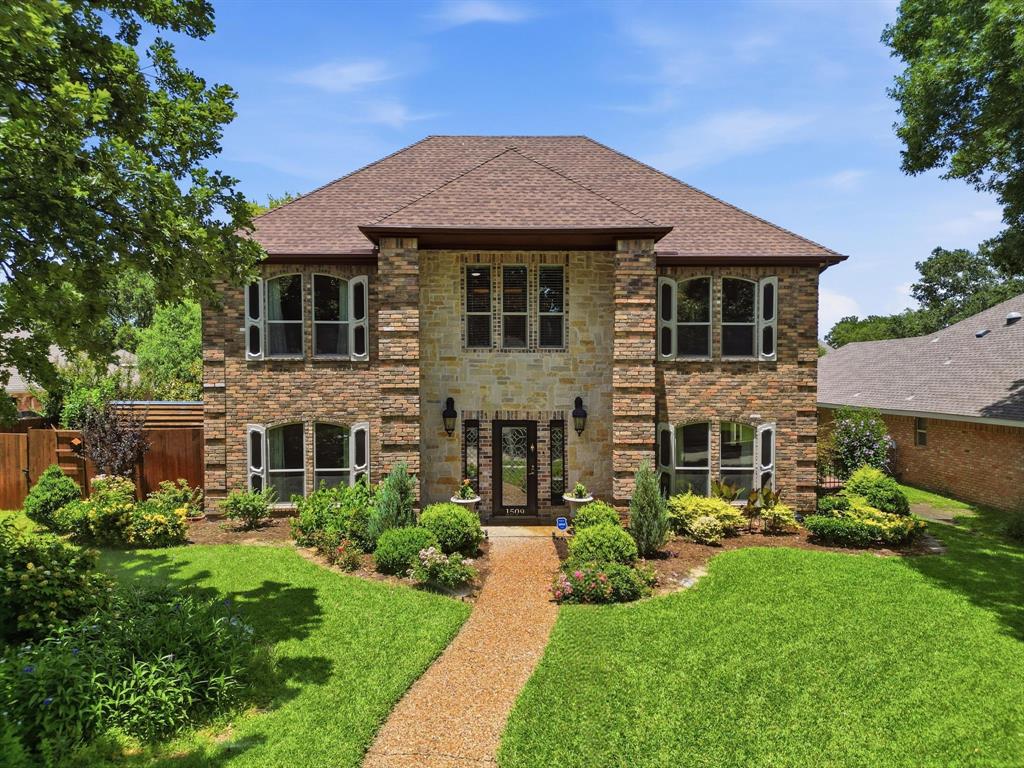 Two-story exterior featuring multi-toned brick and stone masonry, hip roof, arched window detailing, and a stone-paved walkway