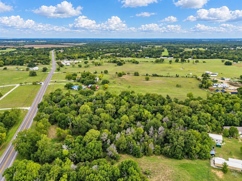Aerial perspective of expansive acreage featuring mature wooded areas, cleared pasture land, and direct frontage to a paved roadway