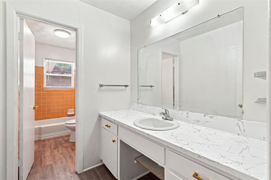 Vanity featuring a white countertop with integrated sink, white cabinetry with gold-finish hardware, and a large wall-mounted mirror