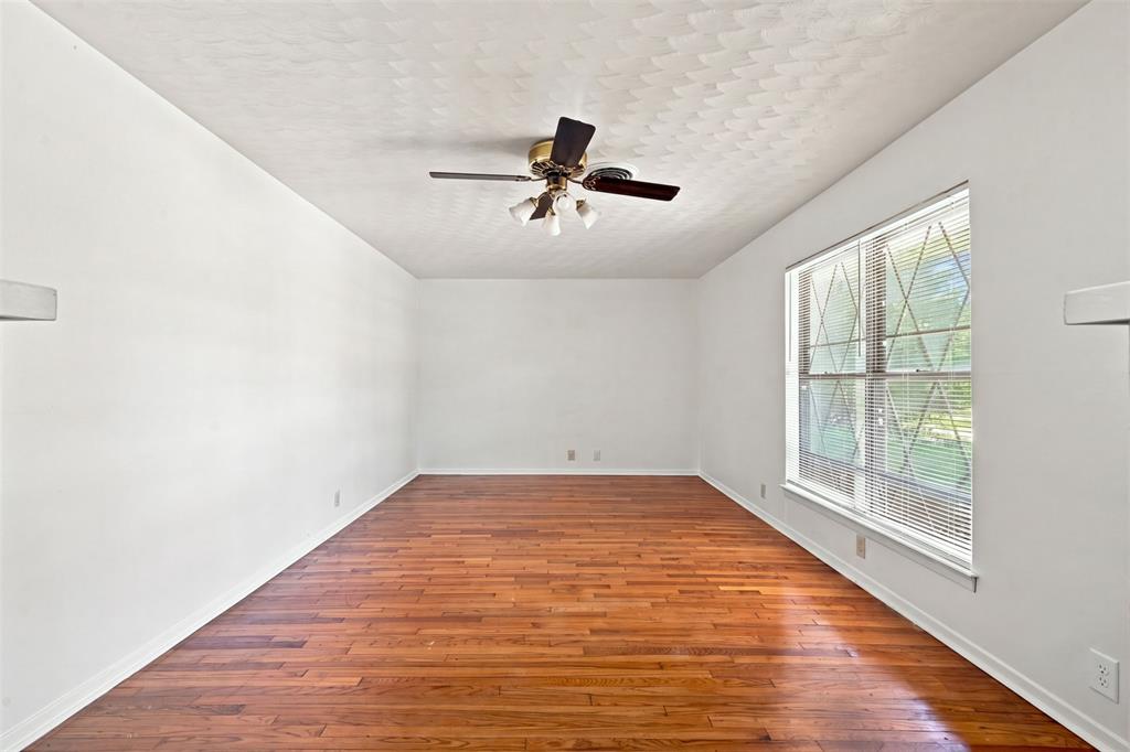 Spacious interior room featuring wood-finish flooring, white walls, and a large window with horizontal blinds