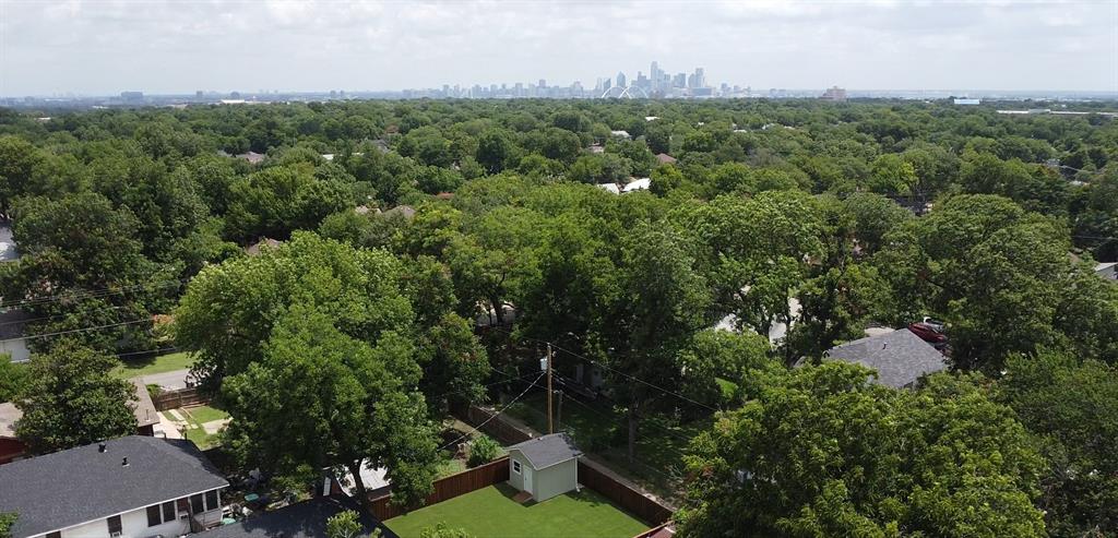 Aerial perspective featuring a backyard with a detached storage structure, enclosed by fencing, set against a backdrop of mature tree canopy and a city skyline