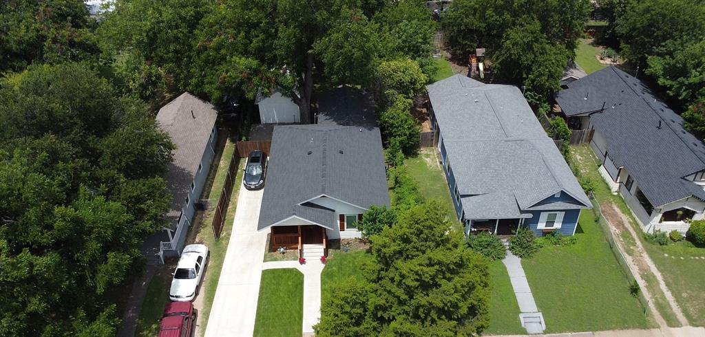 Aerial perspective of a single-story residence featuring a shingled roof, a covered front porch, a concrete driveway, and established mature trees