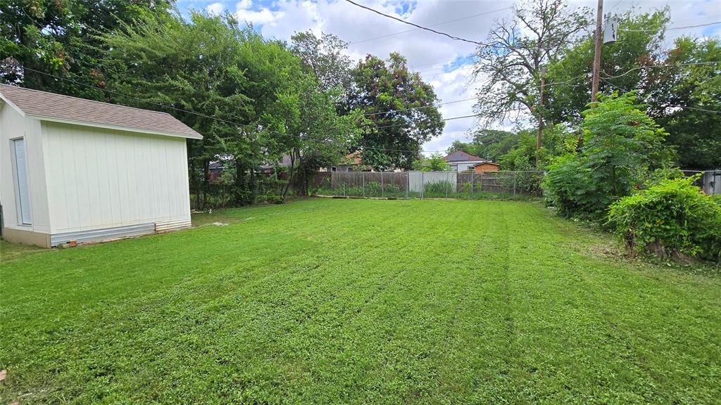 Expansive backyard featuring a level lawn, detached storage shed, perimeter fencing, and mature trees