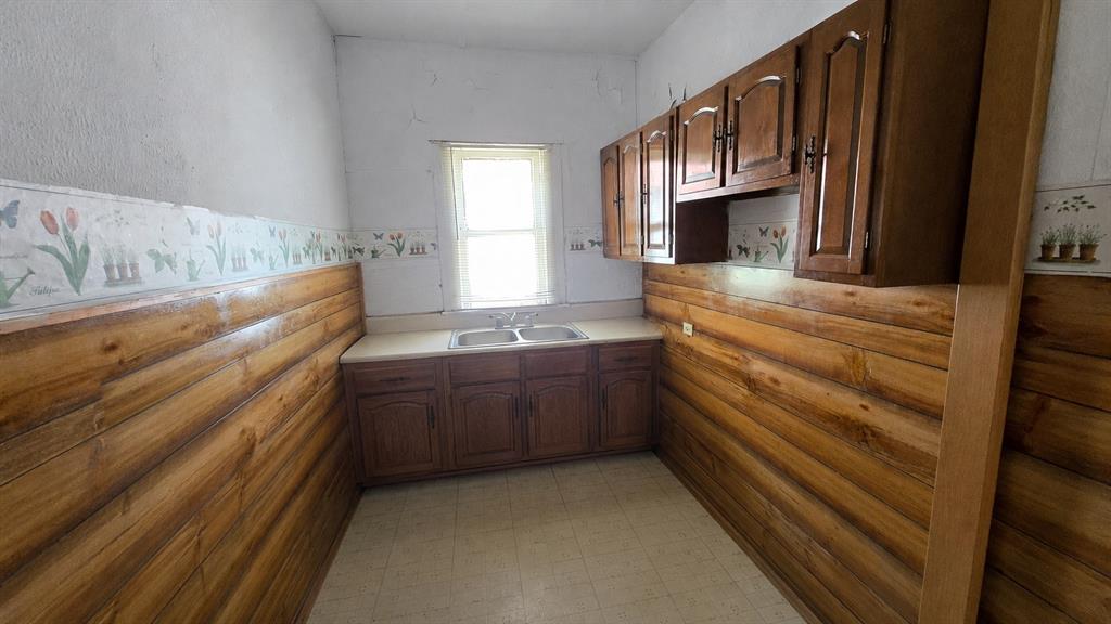 Kitchen featuring wood-paneled walls, built-in upper and lower wood cabinetry, solid-surface countertop, double-basin sink with dual-handle faucet, and tile flooring