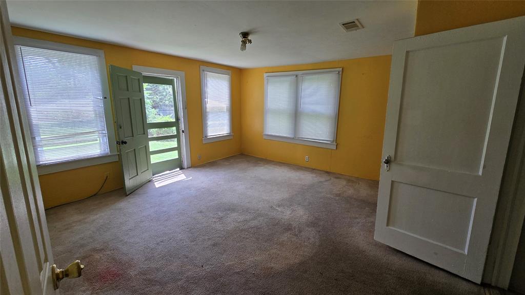 Interior room featuring three double-hung windows, wall-to-wall carpeting, and a multi-pane glass exterior door