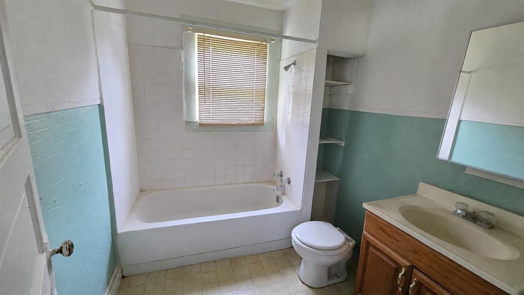 Bathroom featuring a tub-shower combination with tile surround, built-in recessed shelving, a vanity with an integrated sink, and a wall-mounted mirror