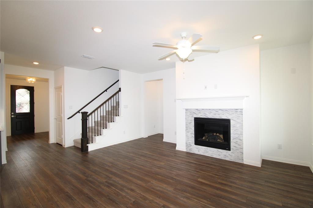 Wood-finish flooring, fireplace with stone-patterned tile surround, fireplace mantel, ceiling fan, and staircase with wooden handrail and balusters