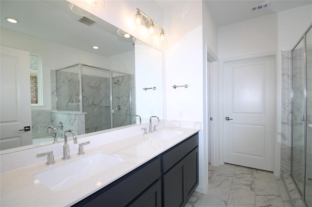 Dual-sink vanity with white countertops, dark cabinetry, polished metal fixtures, full-width mirror, and stone-finish floor tiling