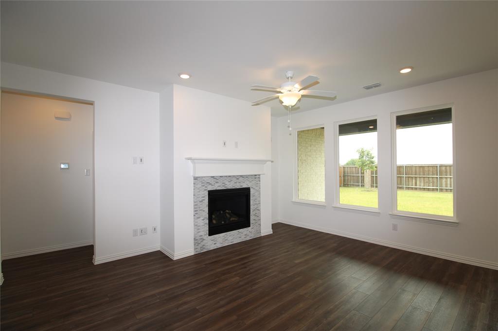 Living area featuring wood-finish flooring, a fireplace with decorative tile surround and a crown-molded mantel, three large windows, and a ceiling fan with integrated lighting