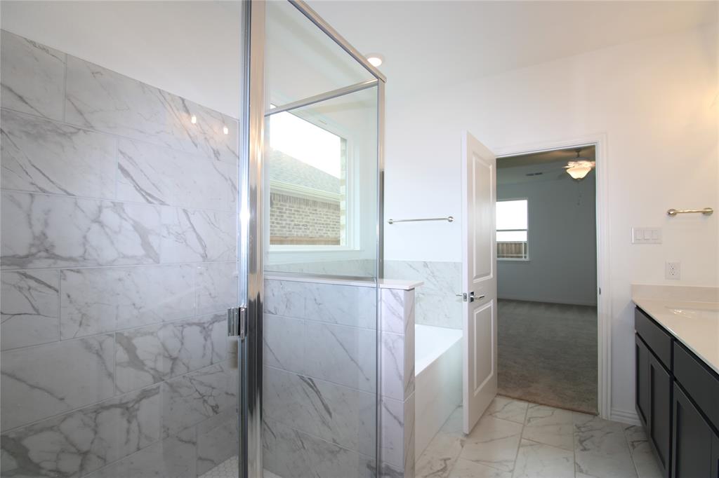 Bathroom featuring a walk-in shower with large-format tile surround, a built-in soaking tub, a dark-finish vanity with a solid-surface countertop, and patterned stone-finish floor tiling