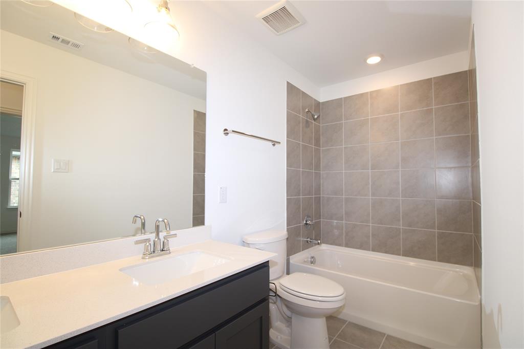 Bathroom featuring a vanity with a white countertop and rectangular undermount sink, large wall-mounted mirror, brushed nickel faucet hardware, and a tub-shower combination with floor-to-ceiling tile surround