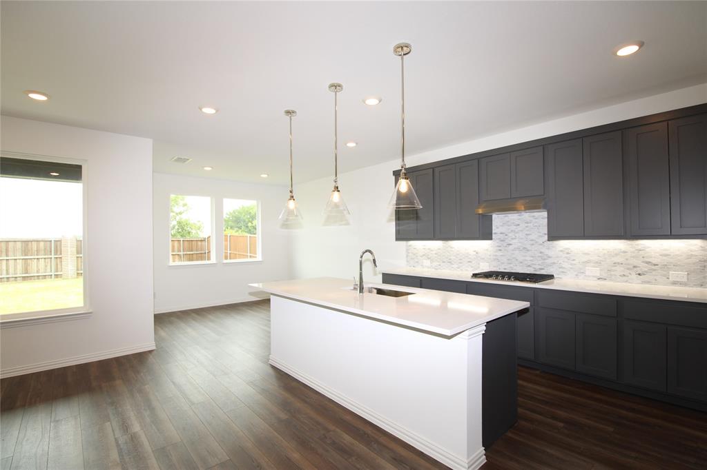 Kitchen featuring dark-toned cabinetry, quartz countertops, a central island with a built-in sink, recessed lighting, and glass pendant fixtures