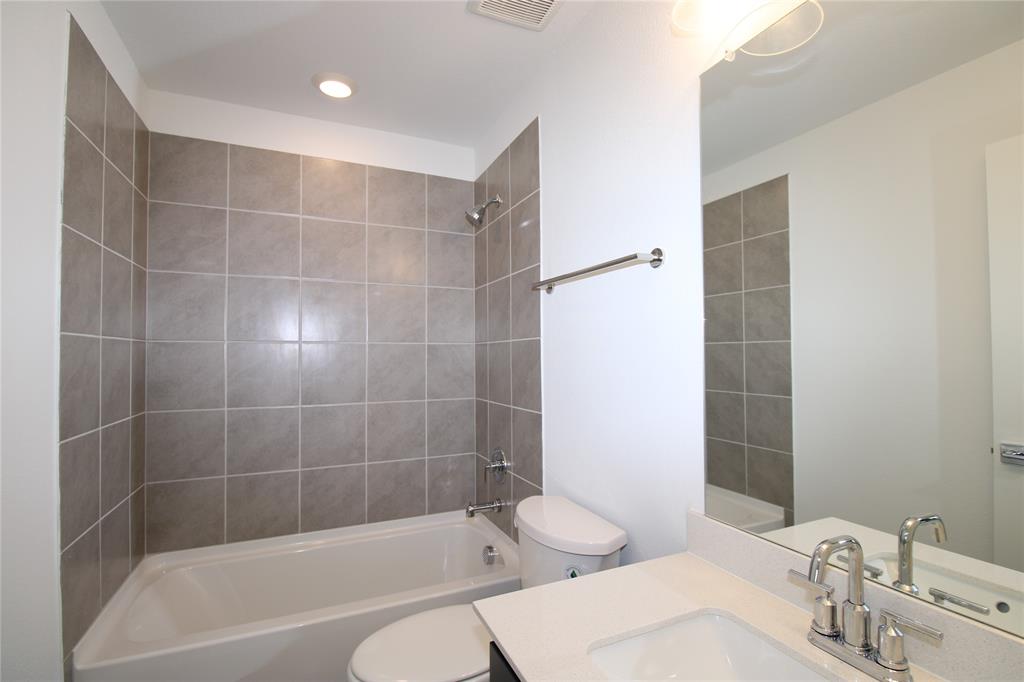 Full-height tile shower surround with integrated tub, vanity featuring a light-toned solid surface countertop, undermount sink with dual-handle chrome faucet, and large wall-mounted mirror