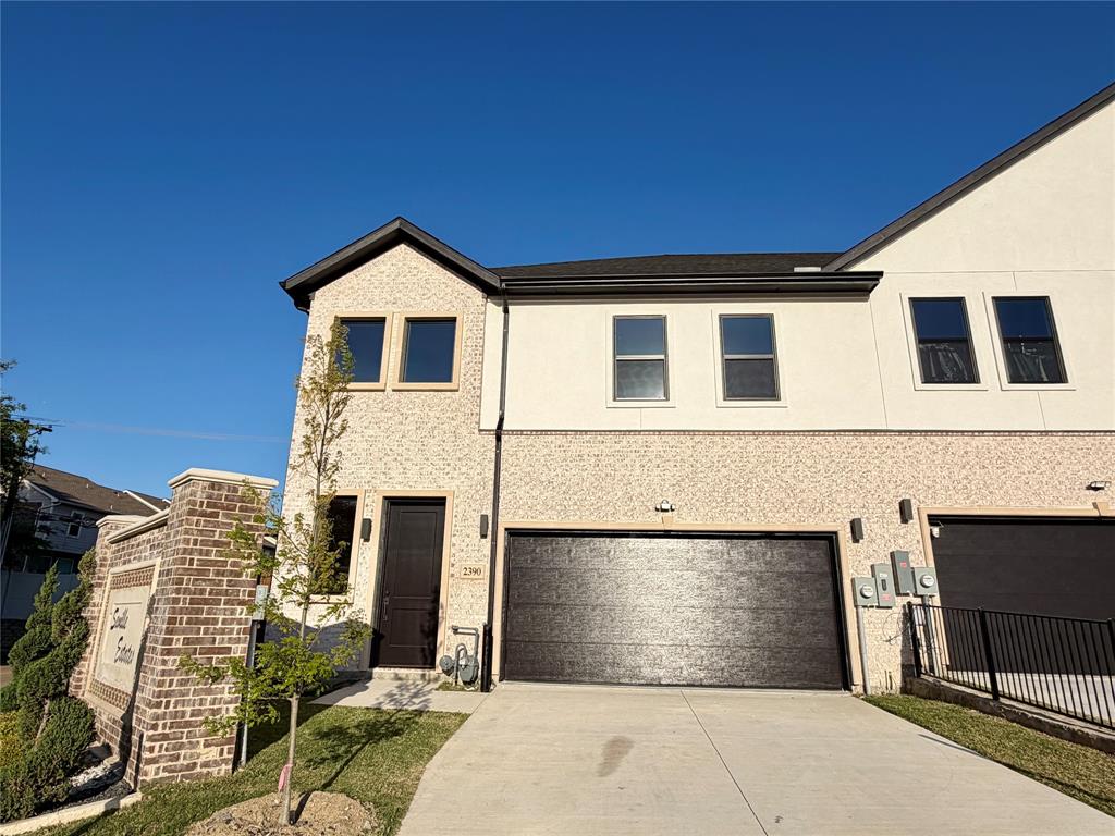 Multi-level exterior featuring a light-toned brick and smooth stucco facade, dual-pane windows, a dark-finish panel entry door, and an attached two-car garage