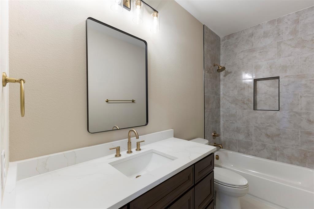 Bathroom featuring a dark wood-finish vanity with a white countertop, rectangular undermount sink, brass-toned fixtures, a framed wall mirror, and a tub with tiled surround and built-in recessed niche