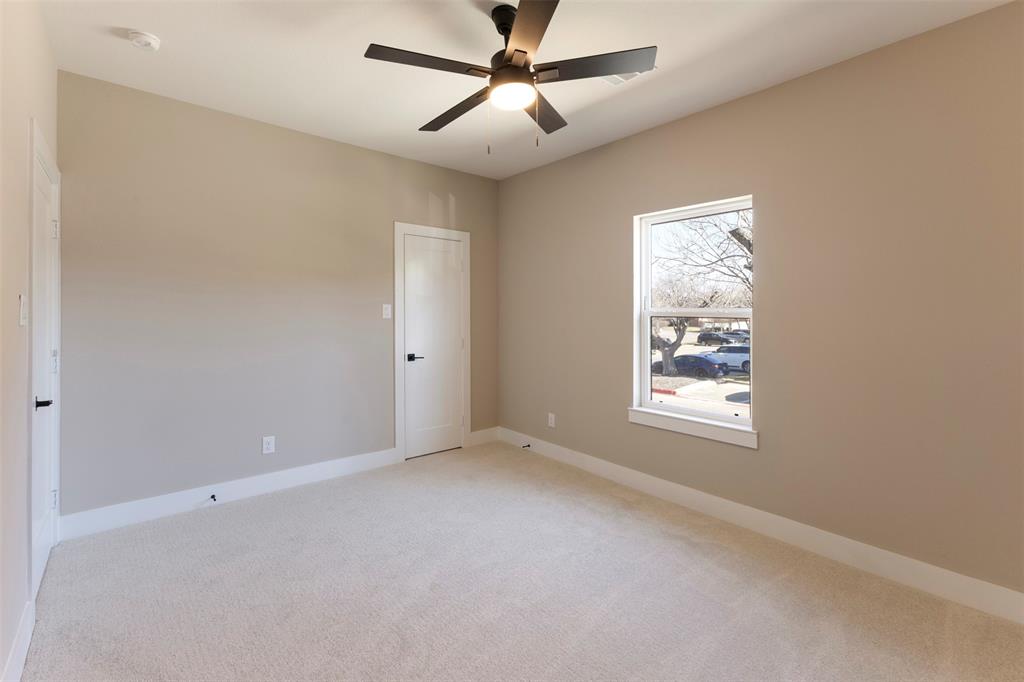 Neutral-toned interior featuring wall-to-wall carpeting, a multi-blade ceiling fan with integrated lighting, and a single-hung window with a wooden sill