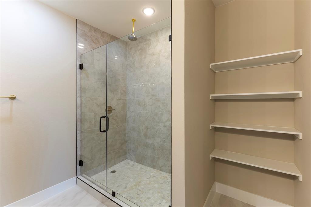 Walk-in shower featuring a glass enclosure, wall-mounted showerhead, and pebble-style floor tiling, complemented by built-in wall shelving