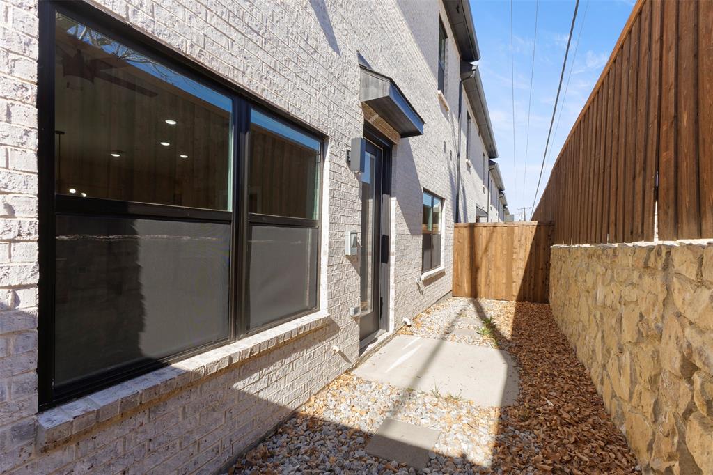 Light-colored brick exterior featuring oversized windows with black frames, a wood privacy fence, and a decorative natural stone retaining wall