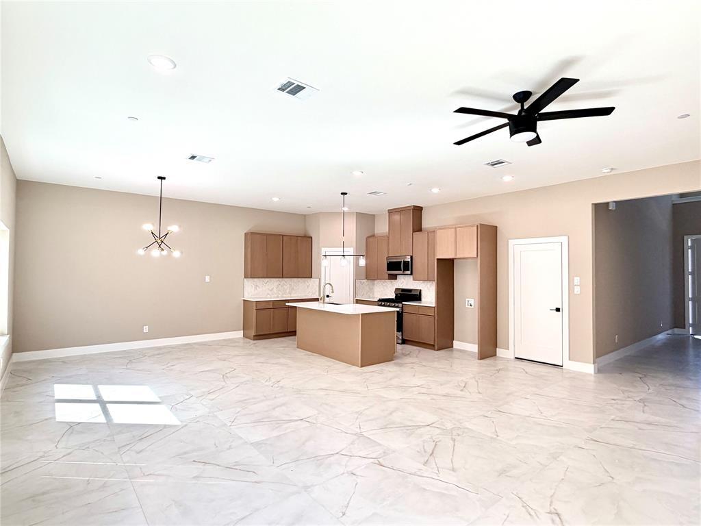 Open concept kitchen featuring flat-panel cabinetry, a central island with a solid surface countertop, stone-finish tile flooring, recessed lighting, and a modern multi-light chandelier
