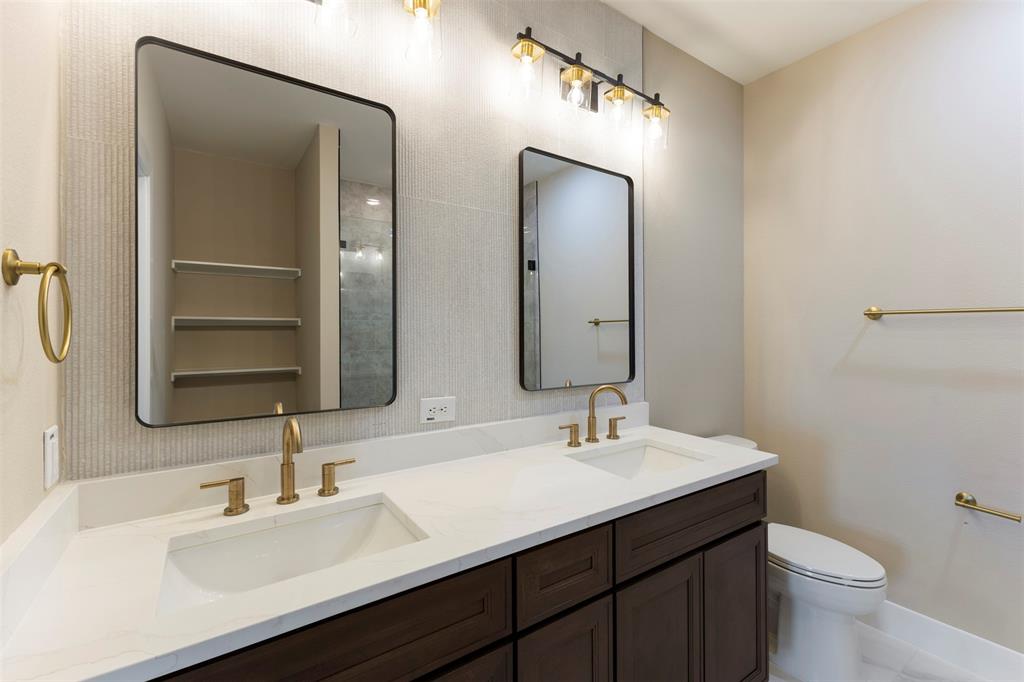 Dual-sink vanity with a quartz countertop, dark wood cabinetry, brass-toned hardware, rectangular mirrors, and linear wall-mounted lighting