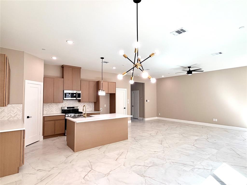Kitchen featuring flat-panel wood cabinetry, quartz countertops, herringbone pattern tile backsplash, stone-finish tile flooring, and a multi-arm geometric chandelier