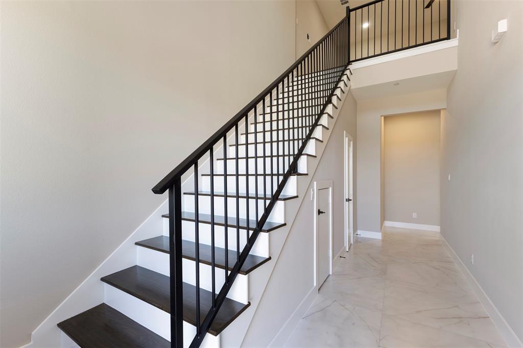 Foyer featuring high ceilings, large-format tile flooring, and a staircase with dark-finish treads and a metal spindle railing