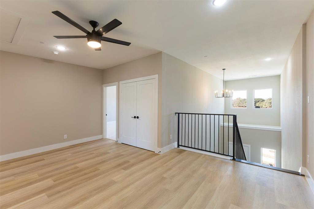Open-concept space featuring light wood-finish flooring, a contemporary matte black ceiling fan, double-door closet, metal baluster railing, and a tiered chandelier
