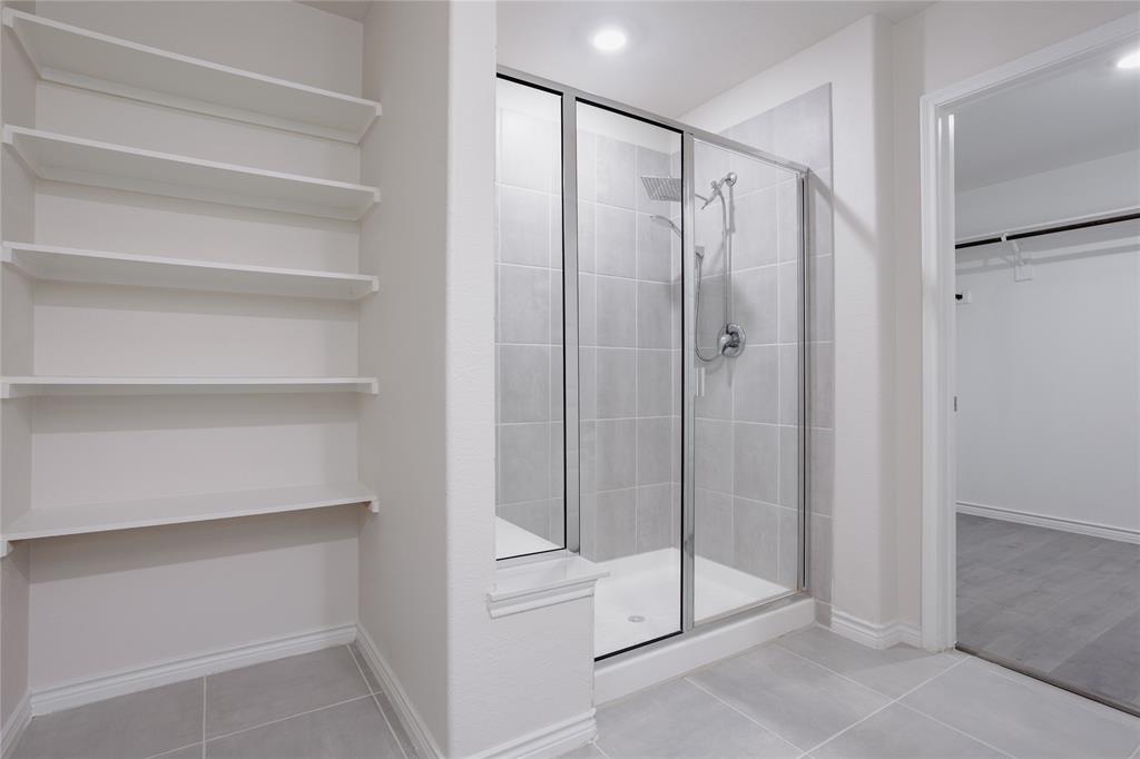 Walk-in shower featuring a glass enclosure, square tile surround, and adjustable handheld shower head, complemented by built-in wall shelving and large-format floor tile