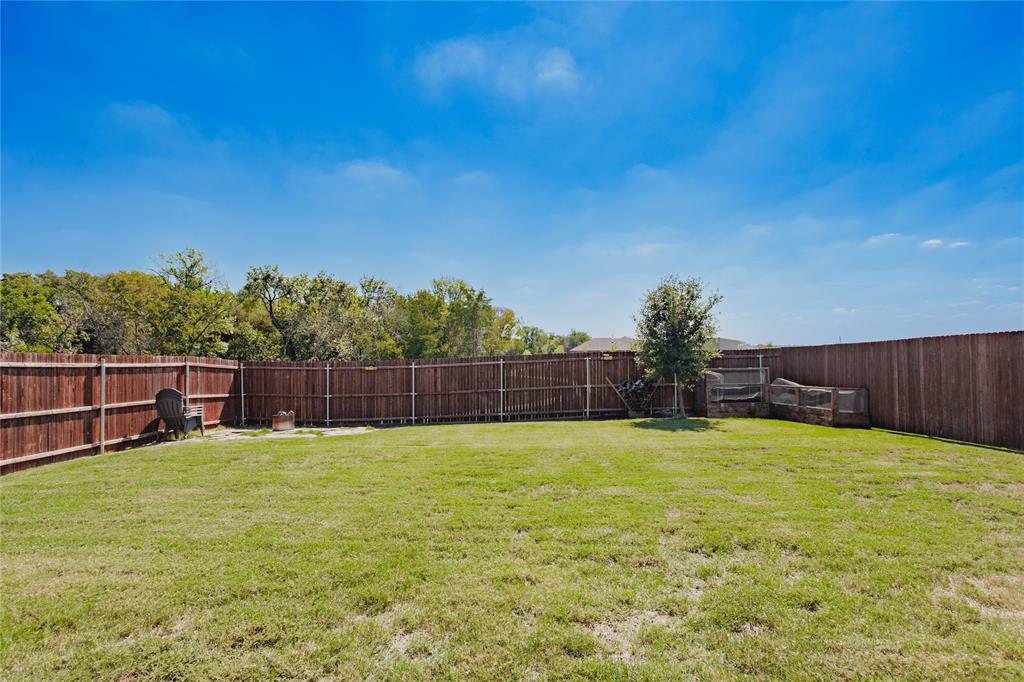 Spacious backyard featuring a manicured lawn, full-perimeter wood privacy fencing, and mature trees