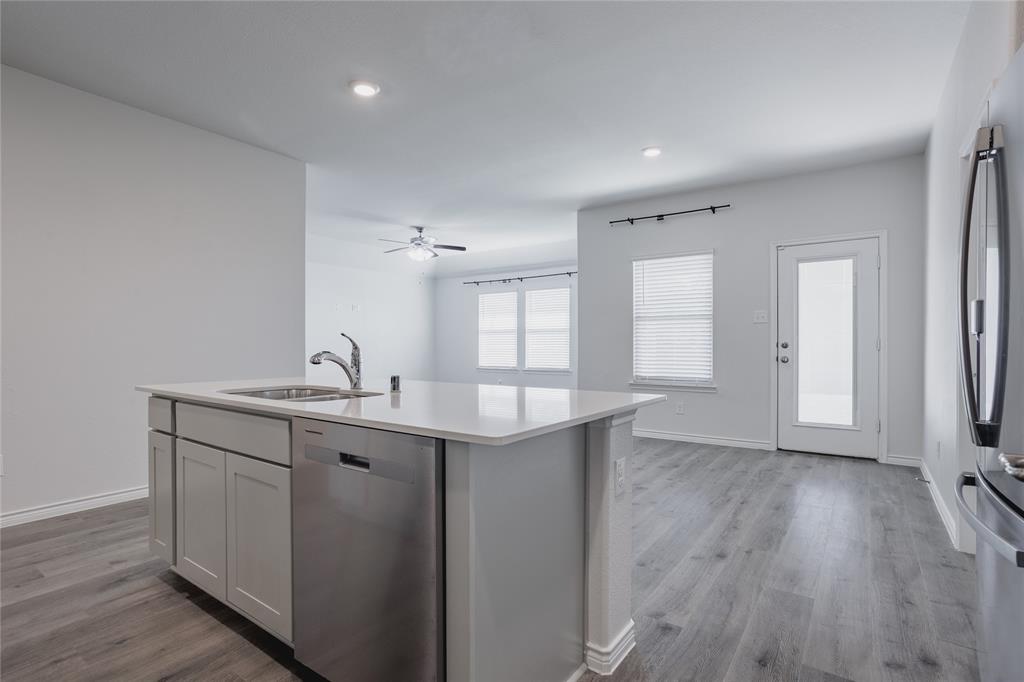 Kitchen island with solid-surface countertop and stainless steel dishwasher, light-toned cabinetry, wood-finish flooring, and recessed lighting