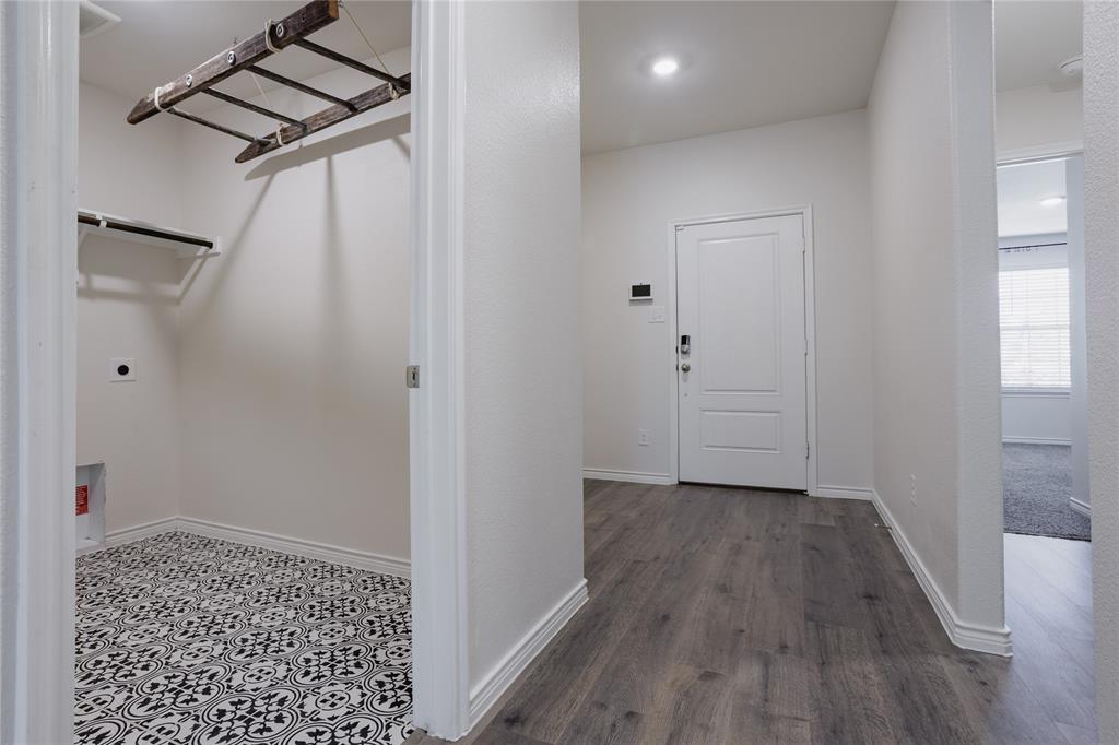 Laundry area featuring patterned tile flooring and a ceiling-mounted wooden drying rack, with wood-finish flooring in the hallway and a panelled entry door Laundry area featuring patterned tile flooring and a ceiling-mounted wooden drying rack, with wood-finish flooring in the hallway and a panelled entry door
