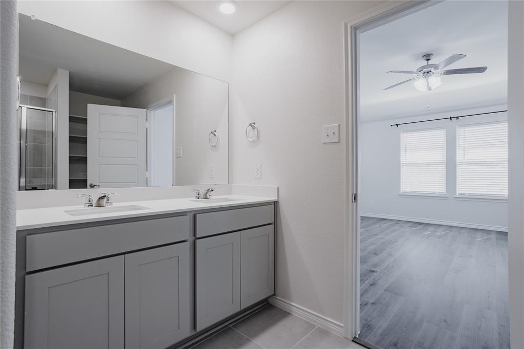 Dual-sink vanity with light-toned countertop, large wall-spanning mirror, grey cabinetry, and wood-finish flooring throughout the space