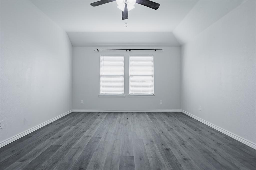 Vaulted ceiling with a centrally mounted ceiling fan, neutral wall finishes, wood-finish flooring, and dual windows featuring adjustable blinds