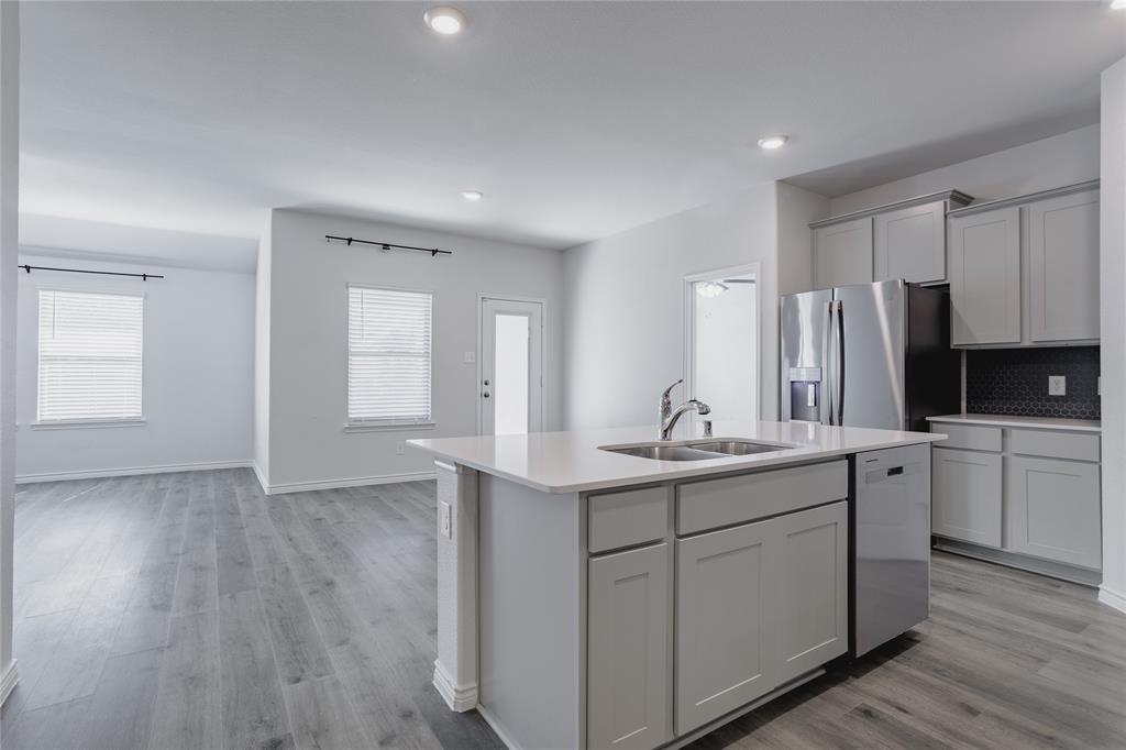 Kitchen featuring a central island with a quartz countertop, stainless steel appliances, grey cabinetry, and wood-finish flooring Kitchen featuring a central island with a quartz countertop, stainless steel appliances, grey cabinetry, and wood-finish flooring