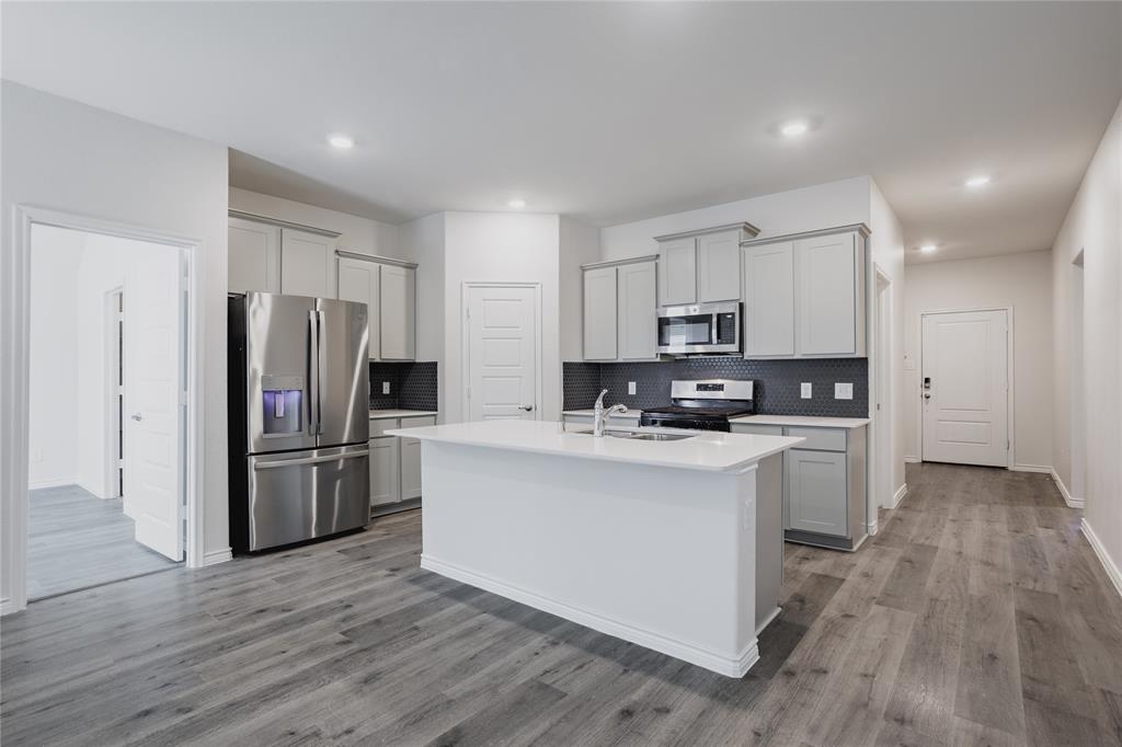 Kitchen featuring a central island with a quartz countertop, stainless steel appliances, light gray cabinetry, a dark tiled backsplash, and wood-finish flooring Kitchen featuring a central island with a quartz countertop, stainless steel appliances, light gray cabinetry, a dark tiled backsplash, and wood-finish flooring