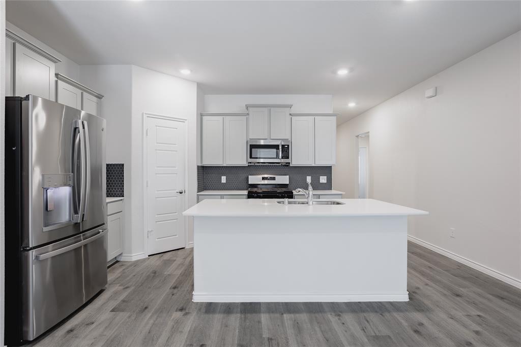 Kitchen featuring a central island with a solid surface countertop, stainless steel appliances, Shaker-style cabinetry, a geometric tile backsplash, and wood-finish flooring Kitchen featuring a central island with a solid surface countertop, stainless steel appliances, Shaker-style cabinetry, a geometric tile backsplash, and wood-finish flooring