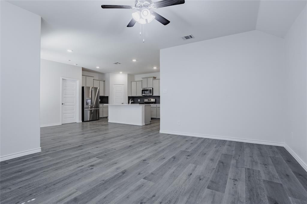 Open-concept interior featuring wood-finish flooring, vaulted ceilings, a kitchen island with stone-surface countertop, recessed lighting, and a ceiling fan with integrated lighting