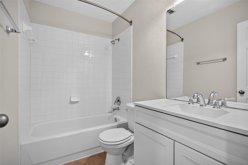 Bathroom featuring a white vanity with a composite countertop, an integrated sink with polished metal fixtures, a large wall-mounted mirror, and a bathtub with a white tile surround