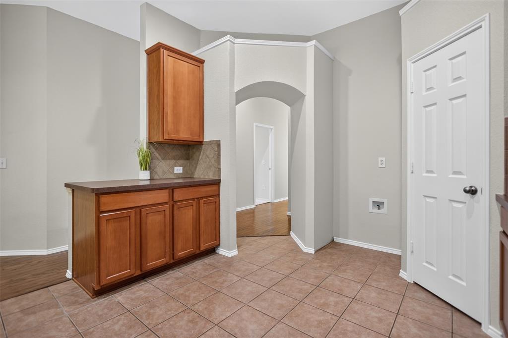 Built-in wood cabinetry with a countertop, tiled backsplash, arched architectural detailing, and tile flooring