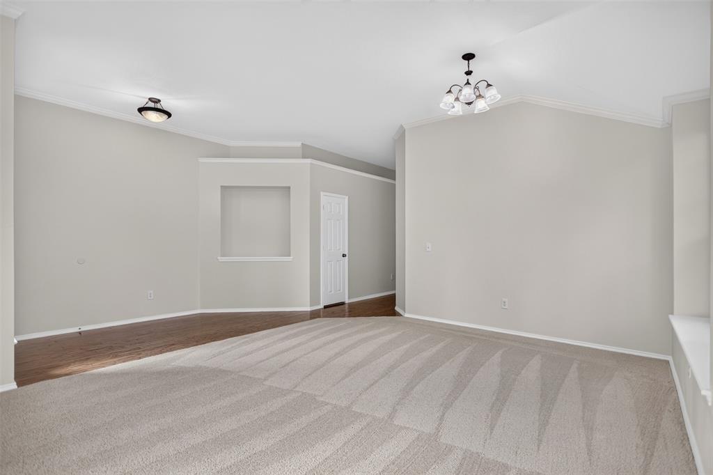 Living area featuring vaulted ceilings, recessed wall niche, neutral carpeting, wood-finish flooring, and multi-light chandelier Living area featuring vaulted ceilings, recessed wall niche, neutral carpeting, wood-finish flooring, and multi-light chandelier